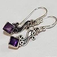Close-up front view of two sterling silver dangle earrings with square purple amethyst stones and scroll design.
