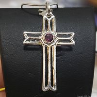 Front angled close-up of sterling silver cross pendant with central round amethyst stone, displayed on black jewelry holder.