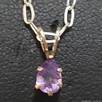 Close-up front view of sterling silver chain and pear-shaped amethyst pendant on black textured background.
