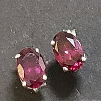 Close-up of two sterling silver stud earrings featuring oval garnet gemstones on a black surface showing deep red facets and clarity of stones.