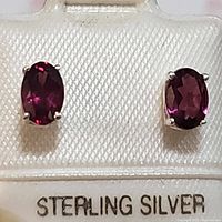 Close-up of both earrings showing the oval red garnet stones set in sterling silver on a textured backing card marked 'STERLING SILVER'.