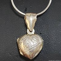 Close-up front view of sterling silver heart-shaped locket pendant showing engraved leaf and beaded design.