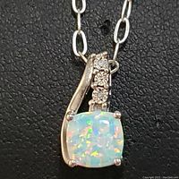 Close-up of pendant showing cushion-cut opalite with prong setting and three small diamonds on the bail, attached to sterling silver chain.