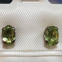 Close-up front view of pair of oval peridot earrings in sterling silver prong settings on display card.