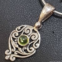 Close-up photo of sterling silver filigree pendant with round green peridot gemstone in center, hanging on a silver snake chain.