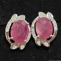 Front view of sterling silver earrings showcasing central oval ruby-colored stones and CZ accents in a decorative setting.