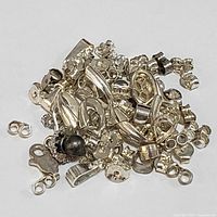 Close-up photo showing assorted sterling silver jewelry parts including bails, clasps, jumprings, and bead caps in a pile on white background.