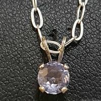 Close-up showing round tanzanite gemstone in four-prong sterling silver setting with part of elongated oval link chain visible.