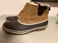 Side view of Eddie Bauer winter boots showing tan leather upper, black rubber foot, and white midsole trim.
