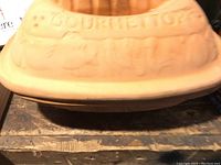 Top view of the Gourmettopf dome lid showing embossed text and decorative patterns with vent holes.