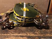 Side view of rolled yellow and black tie down straps with double metal hooks and metal ratchets