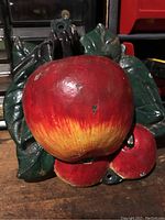 Front view of the metal apple door knocker showing red apple design and green leaves with some paint wear.
