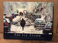 Front cover of 'The Ice Storm' book showing ice storm scene with pedestrian and cars blocked by fallen ice-covered branches on road.