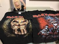 Two black Iron Maiden T-shirts laid flat showing detailed Eddie artwork and band logos.