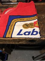 Photo of folded red barbecue apron showing Labatt's detailed branded printed logo with medals and maple leaf symbol.