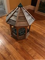 Side view of large wooden bird feeder showing octagonal shape and peaked roof with hanging hook