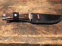 Closed knife with wooden handle and black nylon sheath featuring Coleman label.