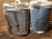 Photo showing two packaged sets of outdoor curtain panels in transparent plastic bags with decoration and product info labels.