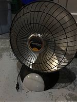 Front view of black Pesto Heat Dish space heater with protective metal grille and white control knob at base.