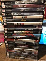 Stacks of PlayStation 2 game cases showing mainly sports and action titles including Tony Hawk's Underground, NHL 06, Gran Turismo 4, and others.