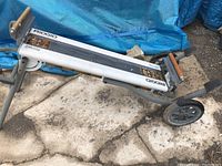 Folded view of the Rigid saw table deck showing metal frame, wheels, and wooden supports on a concrete surface.