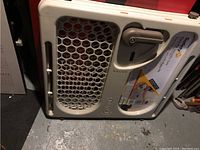 Side view of the beige plastic security gate panel showing the vented pattern and brand logo.