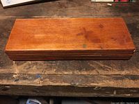 Photo of closed medium-brown wooden box with visible wood grain and simple finish, on a wooden surface.