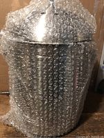 Stainless steel composter fully wrapped in bubble wrap, showing its shiny lid and cylindrical body.