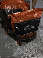 Two unopened bags of Traeger Hickory wood pellets standing on concrete floor.