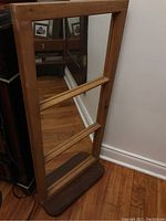 Full view of rectangular wooden framed mirror with three panels and attached dark wood shelf base, standing on hardwood floor, showing rustic finish.
