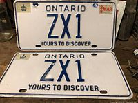 Pair of Ontario ZX1 license plates laid flat showing one plate with a 1989 validation sticker and the other without any sticker.