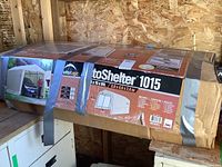 Boxed ShelterLogic AutoShelter 1015 kit packaging on wooden shelf