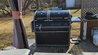 Front view of barbecue grill and smoker combo on wooden deck showing control panel with three knobs, side shelf and rotisserie handle