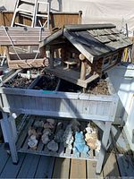 Image of large wooden log home bird feeder on top of the raised herb planter, with animal figurines below on bottom planter shelf