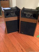 Pair of Bose 301 speakers showing wood side panels, black front grilles, and partially detached speaker foam strips.