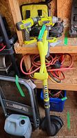 Photo showing Ryobi cordless trimmer, two drills, chargers, and carrying case on shelf with other tools.