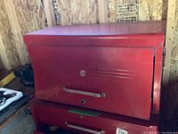 Front view of the closed red metal tool chest showing the handle and dents on top compartment door.