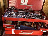 View of top of red toolbox with multiple drawers open, containing many sockets, wrenches, gauges, nozzles, tape measure, plus other small hand tools.