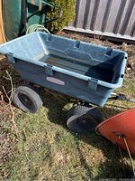 Four-wheeled Rubbermaid garden wagon made of dark blue plastic with air-filled tires, placed on grass outdoors.