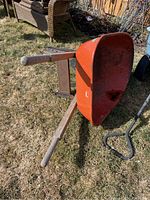 Side and bottom view of the wheelbarrow showing orange metal tray and wooden handles with wear.