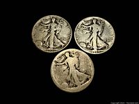 Three Walking Liberty half dollar coins front side laid out on dark surface showing dates 1919, 1936-D and one date illegible