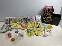 Full lot overview showing loose and sleeved Pokémon cards spread out next to the storage box and game accessories