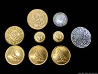 Top-down photo of nine vintage/antique military type buttons on black background showing details.