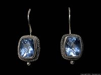 Front view of both sterling silver earrings with blue faceted rectangular stones against a black background showing detailed twisted rope border and small silver ball accent.