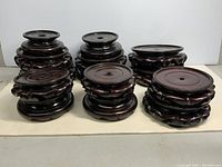 Photo of fourteen Chinese carved wood stands arranged in rows, showing the size variety and detailed wood carvings on bases and tops.