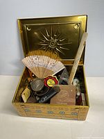 Full view of open decorative metal box showing various vintage items arranged inside including fan, framed portrait, box, and shaver.