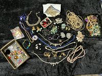 Overall assortment of jewelry findings including chains, beads, pendants, loose stones, and broken pieces on a dark background.