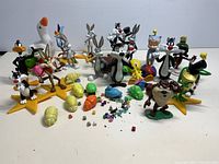 Multiple Looney Tunes character figures arranged standing and in front of others with random small toys in foreground. Figures show various poses and painted details.
