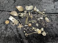 Photo showing the full lot arranged on black cloth with a penny for size reference. Pieces include various broken and mismatched earrings, pendants, filigree flowers, and chain bracelet.