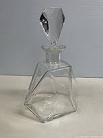 Front view of a clear vintage glass decanter with geometric design and matching glass stopper on top